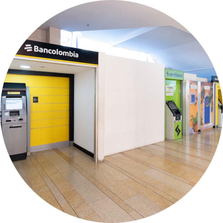 Yellow Bancolombia ATM booth in a shopping center corridor, with additional green Servibanca kiosks to the right.