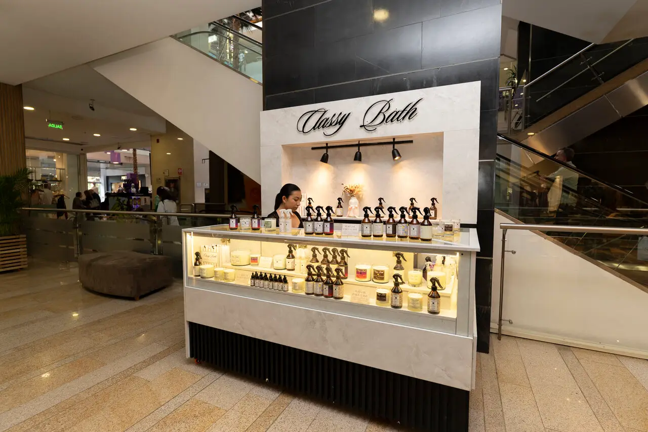 Mall beauty kiosk 'Classy Bath' with a staff member arranging spray bottles and candles in a glass display.