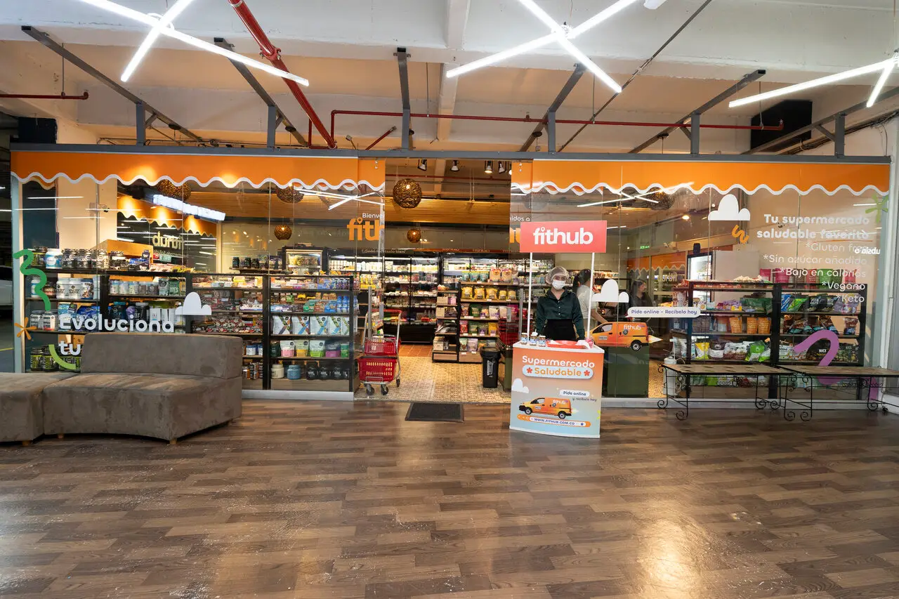 Interior of a health-focused supermarket with shelves of products and a staff member at a front desk near glass doors.