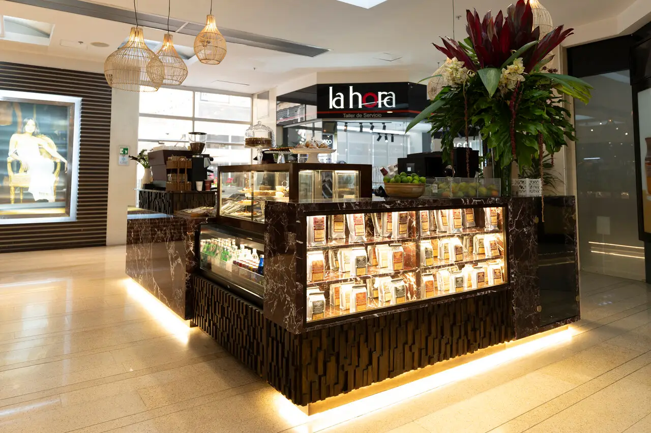 Cafe kiosk inside a shopping mall with a marble counter, glass display of pastries, and warm hanging lights.