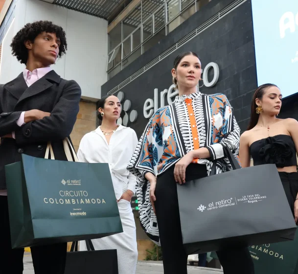 Group of four stylish adults posing with shopping bags on a city street outside a modern building.